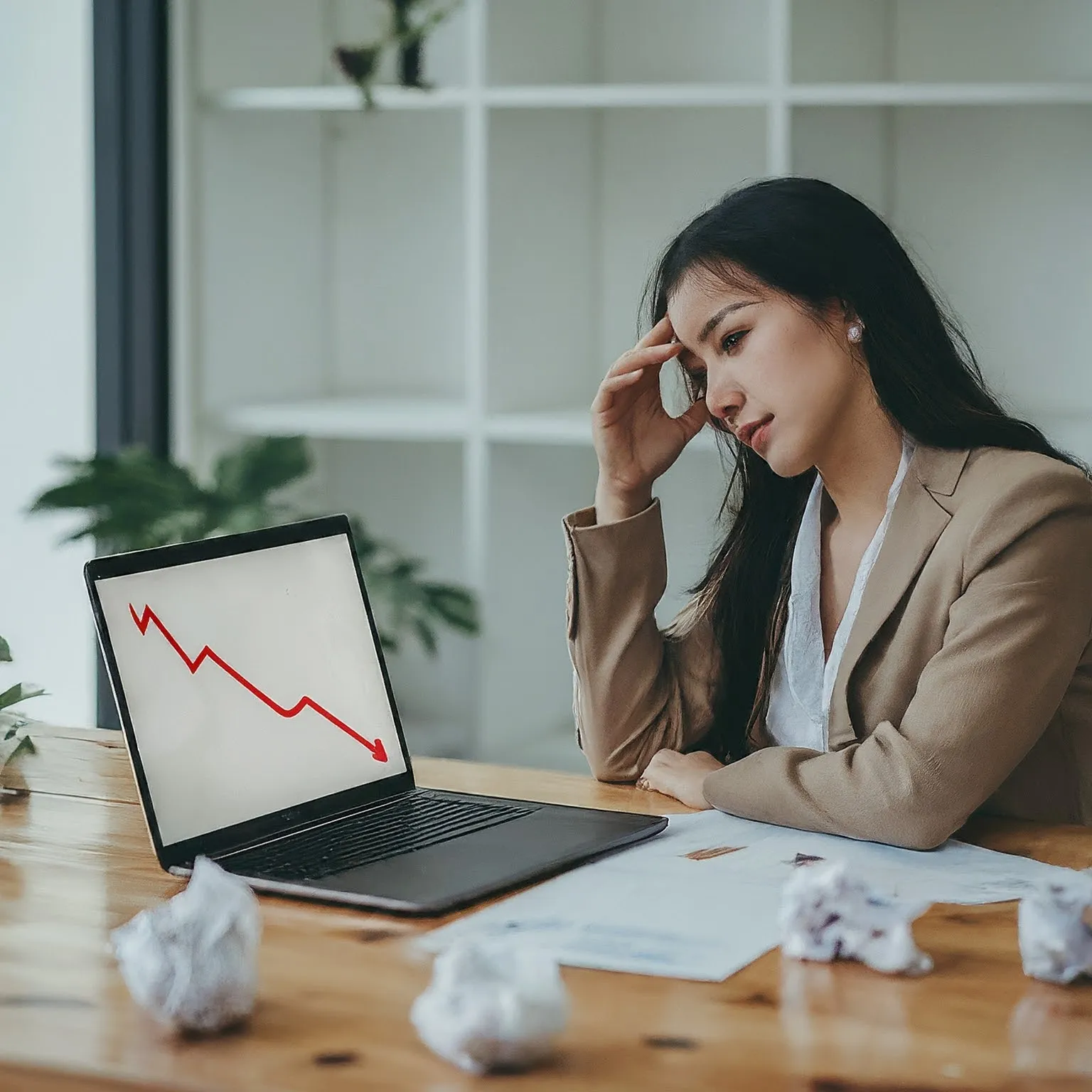 A woman in front of a laptop with arrows going down like a graph.